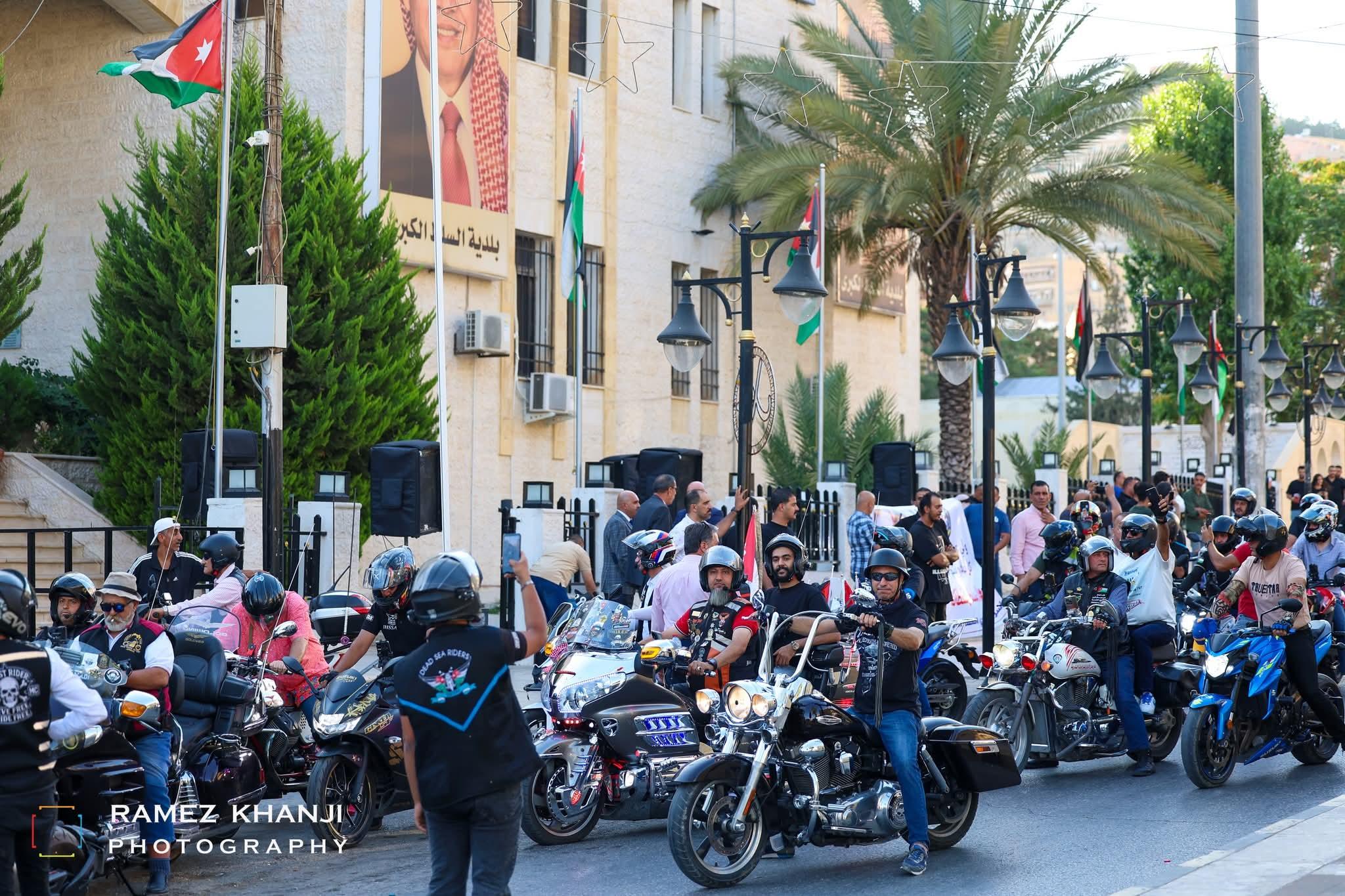 الدراجون ودراجاتهم يحتشدون أمام مبنى البلدية، ولافتة كبيرة ومكبّرات الصوت مهيّأة للفعالية