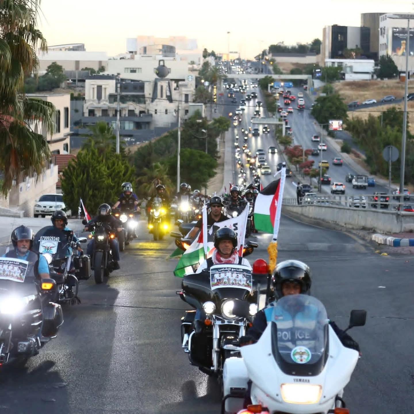 القافلة تنزل منحدرًا في عمّان بمواكبة دورية من الأمن العام، والمدينة وحركة المرور تمتدّان في الخلفية