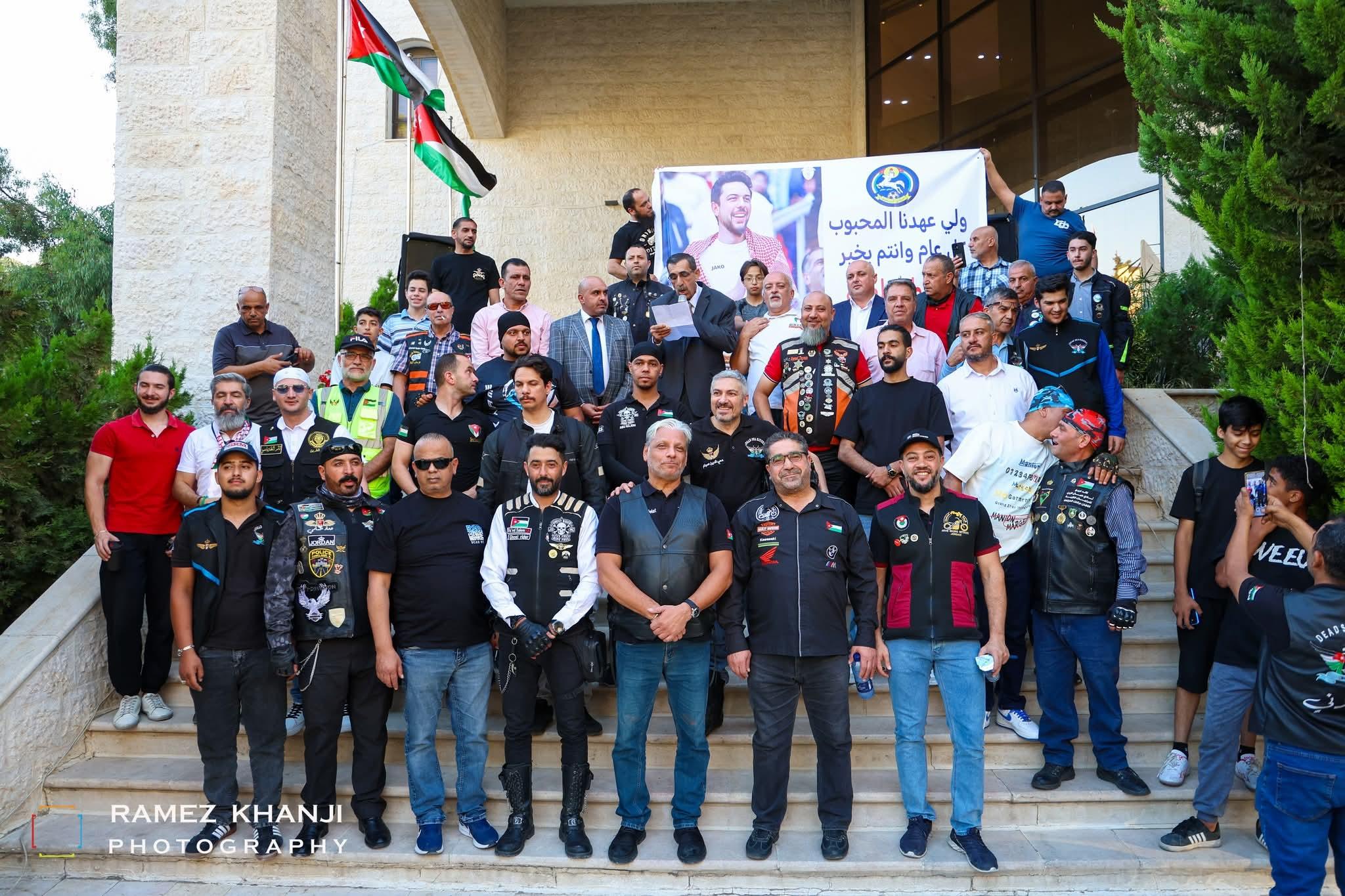 صورة جماعية على درج المبنى وأحد المتحدّثين يقرأ كلمة، وخلفهم لافتة تهنئة لولي العهد