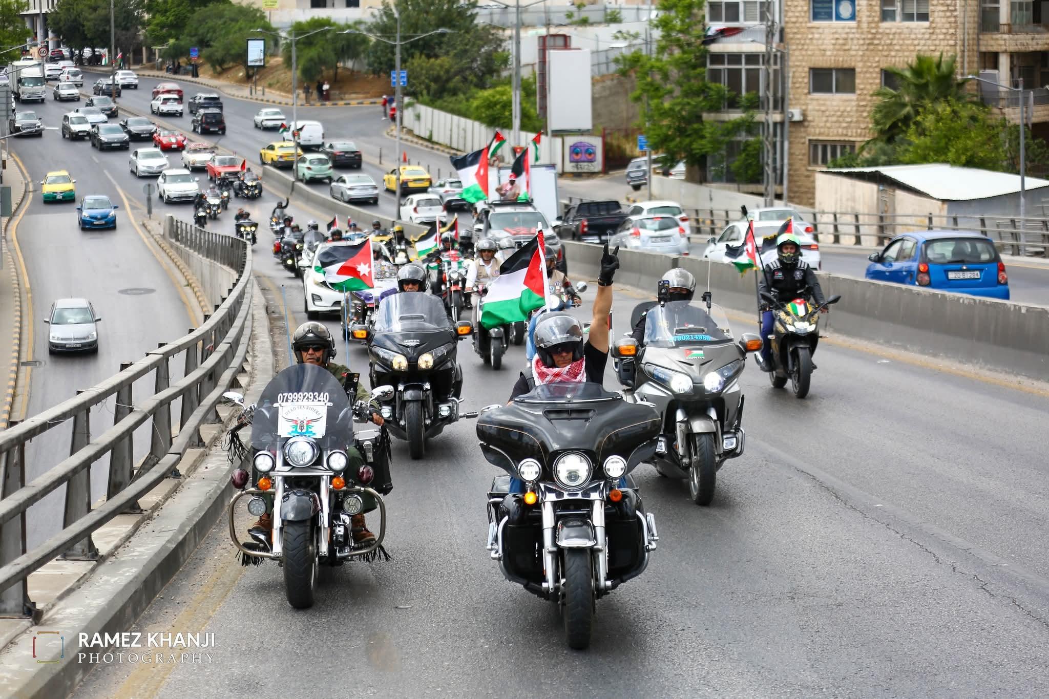 القافلة على طريق مزدوج في عمّان بين صفوف السيارات، والأعلام مرفوعة على الدراجات