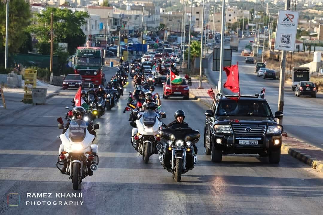 دوريتا شرطة ومركبة مواكبة ترفع الأعلام في مقدّمة القافلة على طريق خارج المدينة