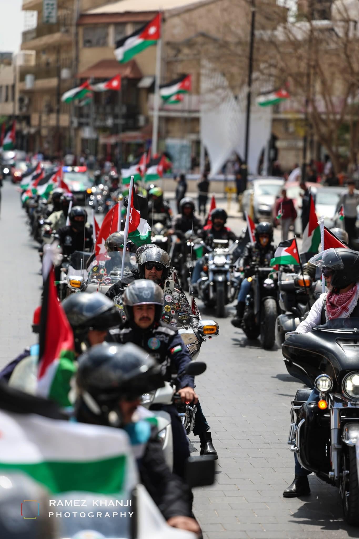 رتل طويل من الدراجات في شارع تحتشد فيه الأعلام الأردنية على الصواري وعلى الدراجات معًا