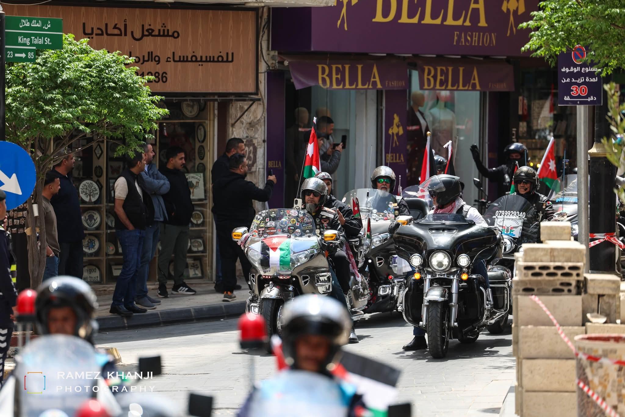 الدراجات تمرّ في شارع الملك طلال أمام مشغل للفسيفساء ومتاجر الشارع، والمارّة يسجّلون بهواتفهم