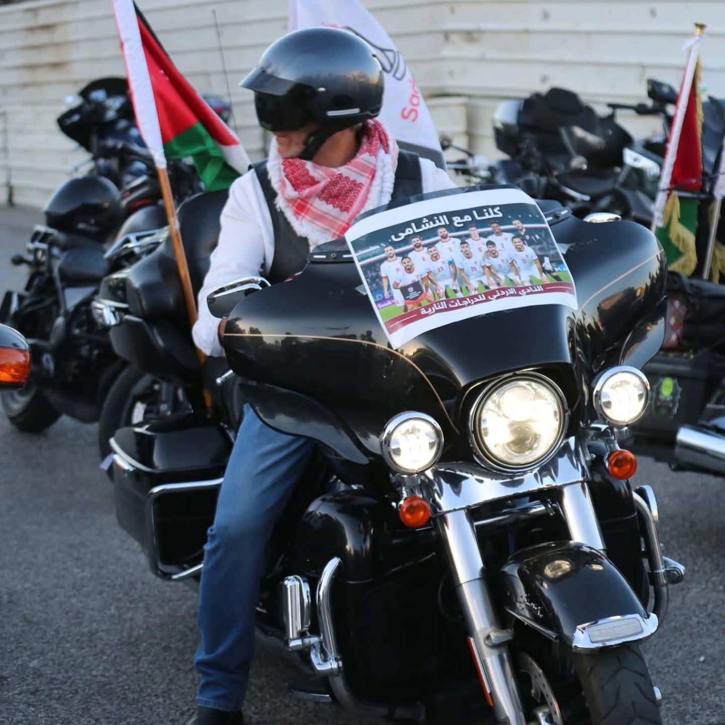 دراج بالشماغ الأحمر على دراجته التي تحمل ملصق مساندة المنتخب الوطني، والعلم الأردني مرفوع إلى جانبه