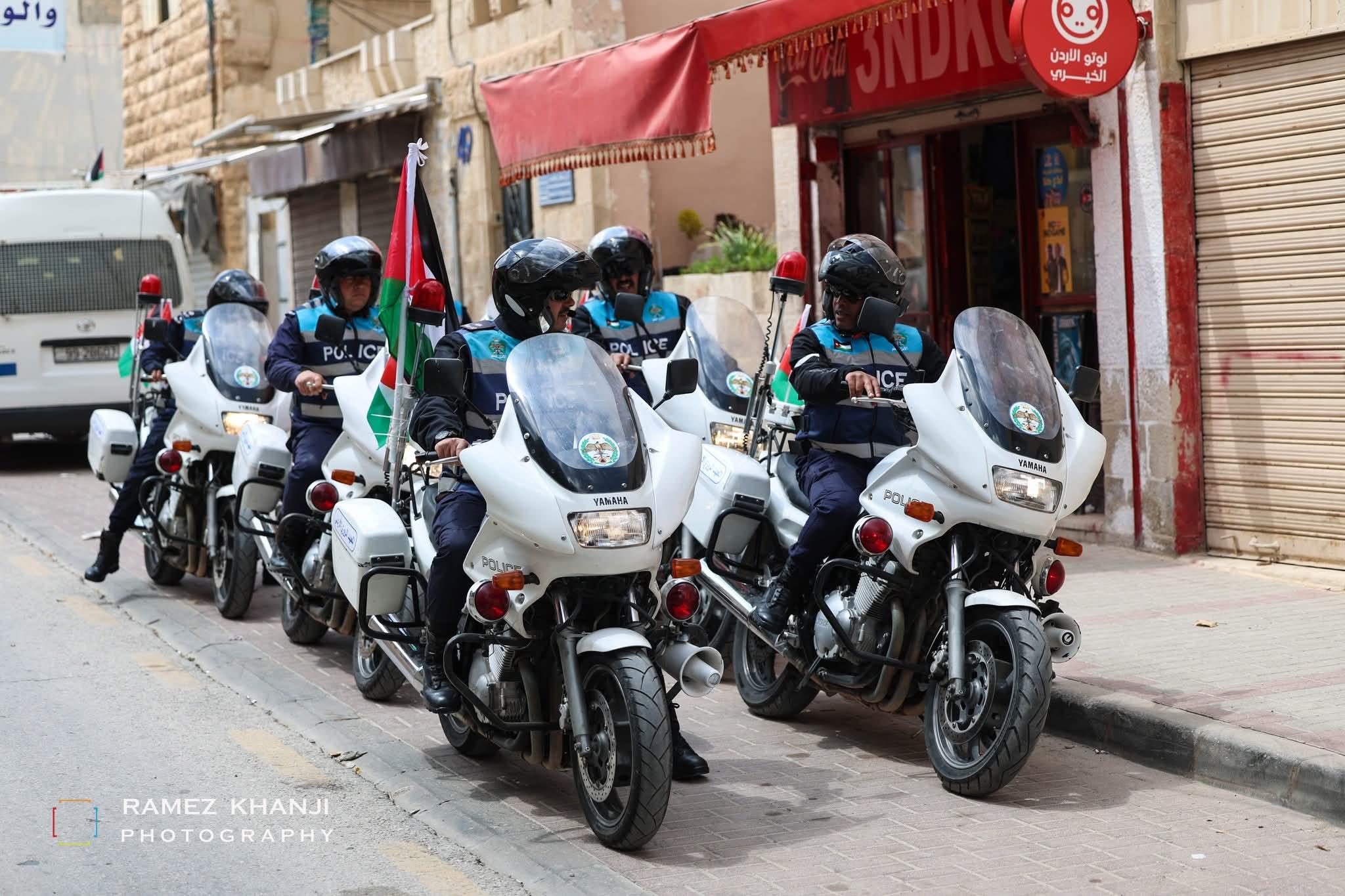 أربع دوريات من الأمن العام تسير على مهل في شارع حجري أمام المتاجر، وعلم أردني على صاري إحداها