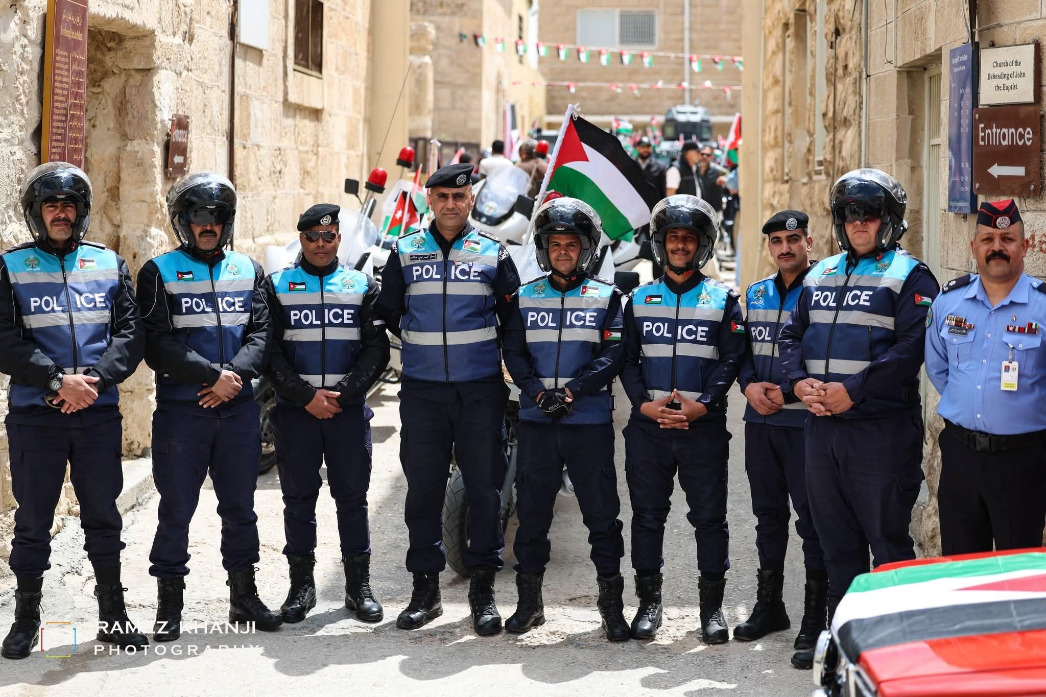 تسعة من ضباط الأمن العام يصطفّون في زقاق حجري أمام دورياتهم، ولافتة كنيسة قطع رأس يوحنا المعمدان إلى جانبهم