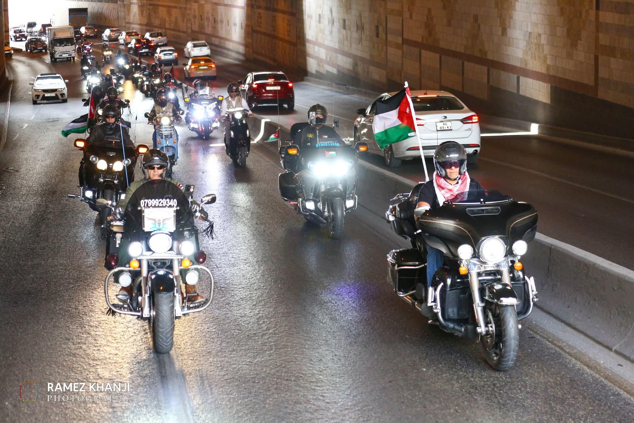 القافلة تعبر نفقًا مكسوًّا بالحجر إلى جانب حركة المرور، وعلم أردني كبير مرفوع على إحدى الدراجات