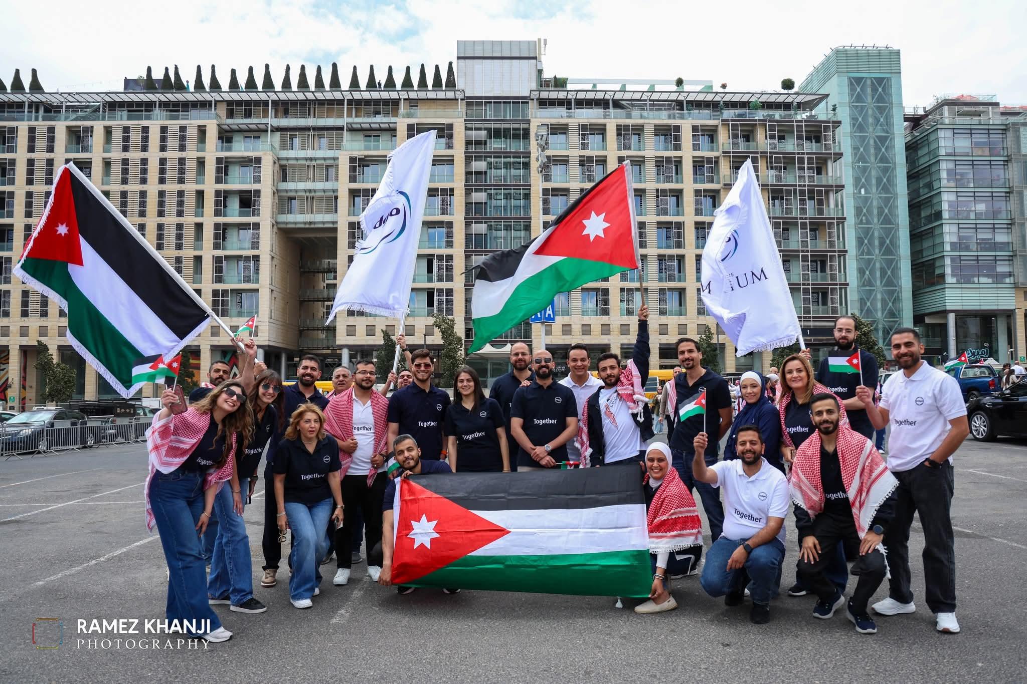 فريق المتطوّعين بقمصان موحّدة يحملون الأعلام الأردنية أمام أبنية العبدلي